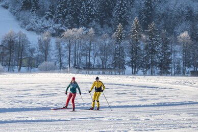 Zwei Langläufer auf präparierter Loipe in winterlicher Landschaft mit verschneiten Bäumen im Hintergrund | © Salzburger_Sportwelt_Lorenz_Masser
