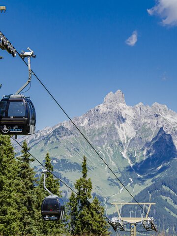Papageno cable cars glide above conifer forest in Filzmoos, with a striking rocky mountain massif behind them. | © filzmoos.ski