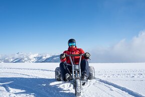 Person fährt mit Mountaincart über verschneites Hochplateau mit Alpenblick bei blauem Himmel in Dorfgastein | © Dorfgasteiner Bergbahnen