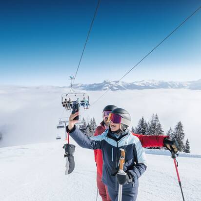 Two skiers take a selfie on sunny slope with chairlift and mountain view in Ski amadé