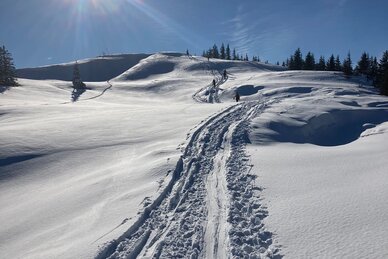Skitourenspur führt durch glitzernden Schnee bergauf, Sonne leuchtet am blauen Himmel