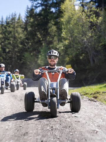 Group rides mountain carts downhill on gravel path through forested alpine terrain | © Dorfgasteiner Bergbahnen AG
