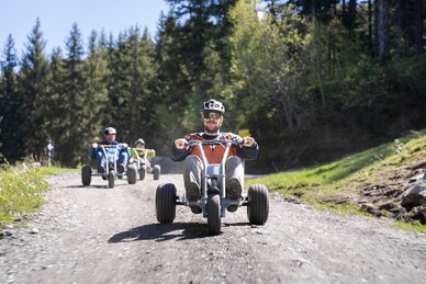 Gruppe fährt mit Mountaincarts rasant bergab auf Schotterweg durch Waldgebie | © Dorfgasteiner Bergbahnen AG