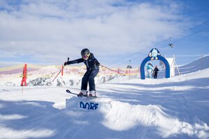 Kind in Skibekleidung springt über Schanze im Übungsbereich mit Skibogen und Sicherheitsnetz in Dorfgastein | © Dorfgasteiner Bergbahnen