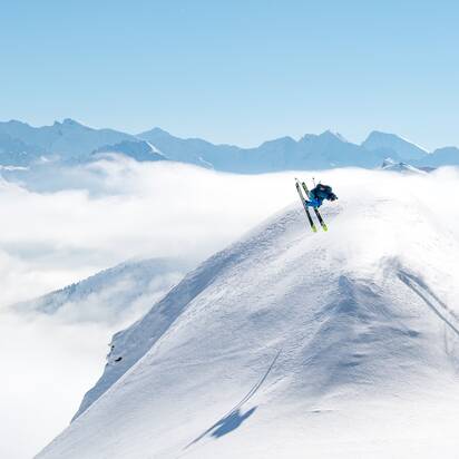 Skifahrer mach einen Backflip über eine Schneekuppel und rundherum sind verschneite Berge und ein blauer Himmel zu sehen | © Gasteinertal Tourismus GmbH, www.oberschneider