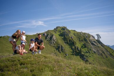 Family with three children rests on meadow at Schlossalm in Gastein, looking at mountains and cable cars | © Balazs Kovacs