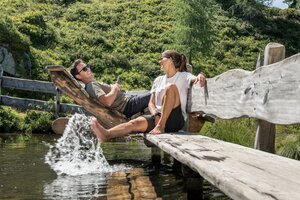 Paar entspannt auf Holzliegen und kühlt die Füße im Wasser am Graukogel | © Skigastein, seven frames