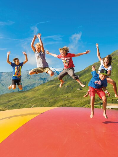 Kinder springen auf buntem Hüpfkissen am Spielplatz Schlossalm mit Bergblick und Sommerstimmung | © Gasteiner Bergbahnen AG, Wolkersdorfer