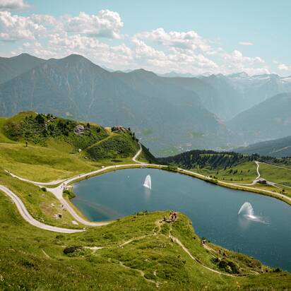 Speichersee auf der Schlossalm mit Wasserfontänen, umgeben von Wanderwegen und Almlandschaft in Gastein | © Gasteiner Bergbahnen AG