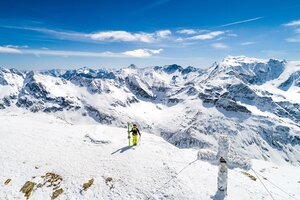 Freeskier steht neben einem frostigen Gipfelkreuz und hält die Ski in einer und die Stöcke in der anderen Hand | © Christoph Oberschneider