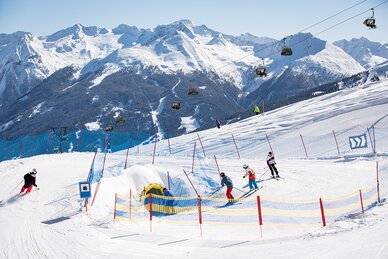 Vier Personen fahren auf einer Funslope in Richtung eines Tunnels und im Hintergrund sieht man eine Piste | © Roland Haschka