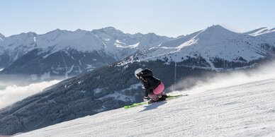 Skifahrerin in Kurve auf Piste mit Blick auf verschneite Wälder und Berge | © Simon Hutter