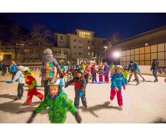 Viele Kinder und ein paar Erwachsene tummeln sich auf einem Eislaufplatz