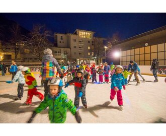 Viele Kinder und ein paar Erwachsene tummeln sich auf einem Eislaufplatz