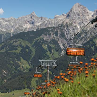 Orange chairlifts of Hochmaisbahn float above alpine slopes and blooming meadows in summer near Hochkönig. | © Roland Haschka