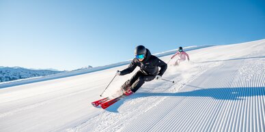 Zwei Skifahrer auf perfekt präparierten Pisten in strahlendem Sonnenschein in der Skiregion Hochkönig bei Maria Alm – Winterspaß und Naturerlebnis pur.  | © Hochkönig Tourismus GmbH