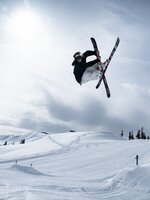 A freestyler jumps over a jump in Kings Park and does a trick with crossed skis.