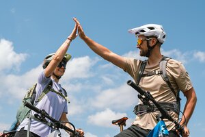 Two mountain bikers give each other a high five on their bikes under a blue sky with scattered clouds | © Hochkönig Bergbahnen