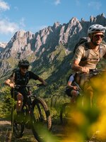 Three mountain bikers ride in Mühlbach on a trail in front of a steep rocky massif near Karbachalmbahn. | © Hochkönig Bergbahnen