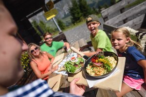 A server brings a dish with salad to a family on the sunny terrace at Karbachalm in Mühlbach. | © Hochkönig Bergbahnen
