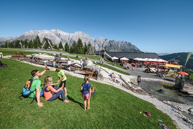 Families enjoying the water playground at Karbachalm with stunning Hochkönig backdrop on a sunny mountain day