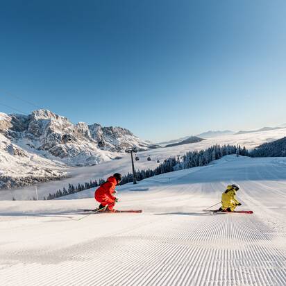 Two skiers at sunrise on freshly groomed slope in Mühlbach with alpine backdrop | © Hochkönig Tourismus GmbH