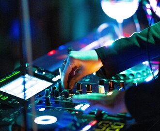 Nahaufnahme einer Hand am Mischpult mit bunten Lichtern bei DJ-Auftritt auf Nachtfestival