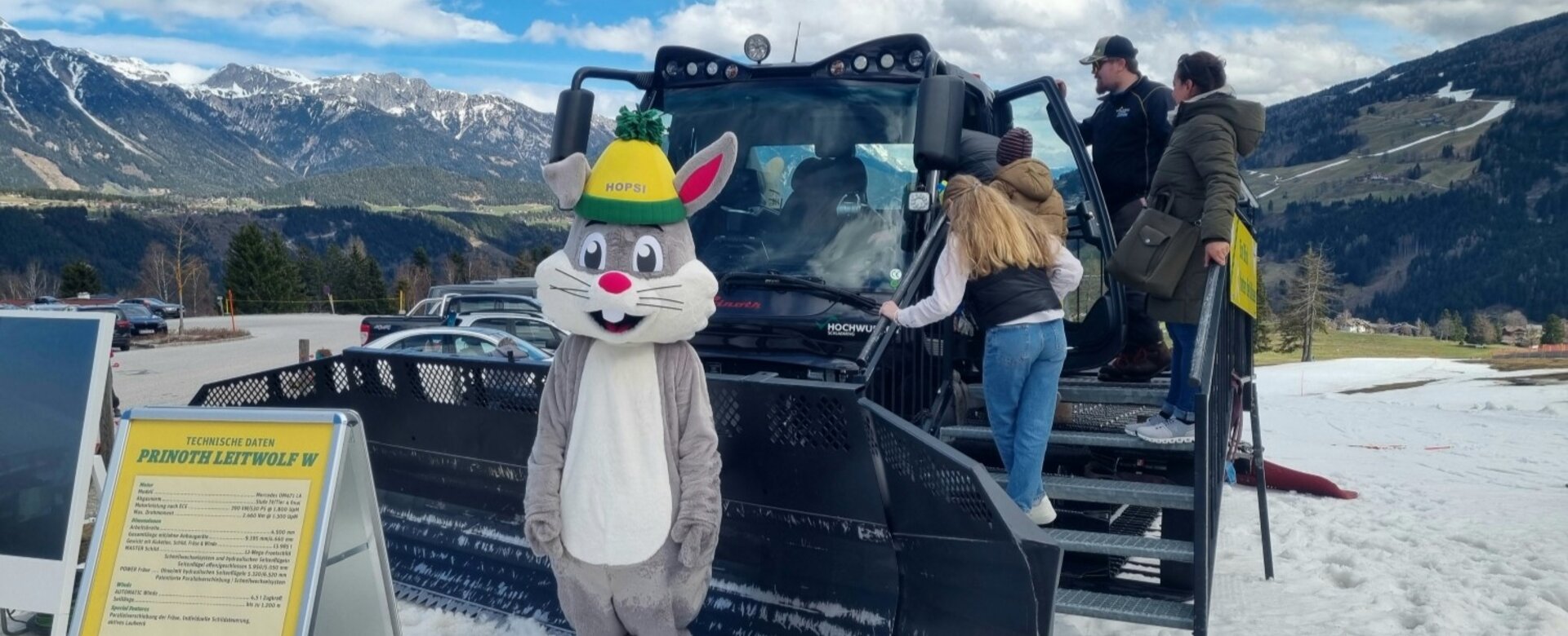 Das Maskottchen Hopsi steht vor dem Pistengerät während ein paar Leute es sich ansehen | © Dagmar Neureiter