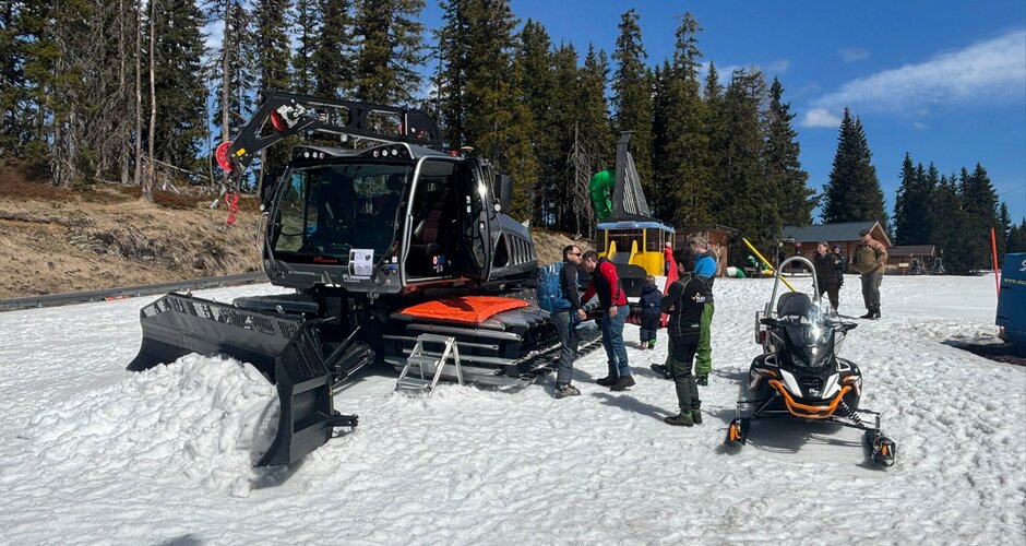 Mehrere Personen stehen im Schnee neben einer Pistenraupe und einem Schneemobil vor Waldkulisse bei Sonnenschein | © Planai