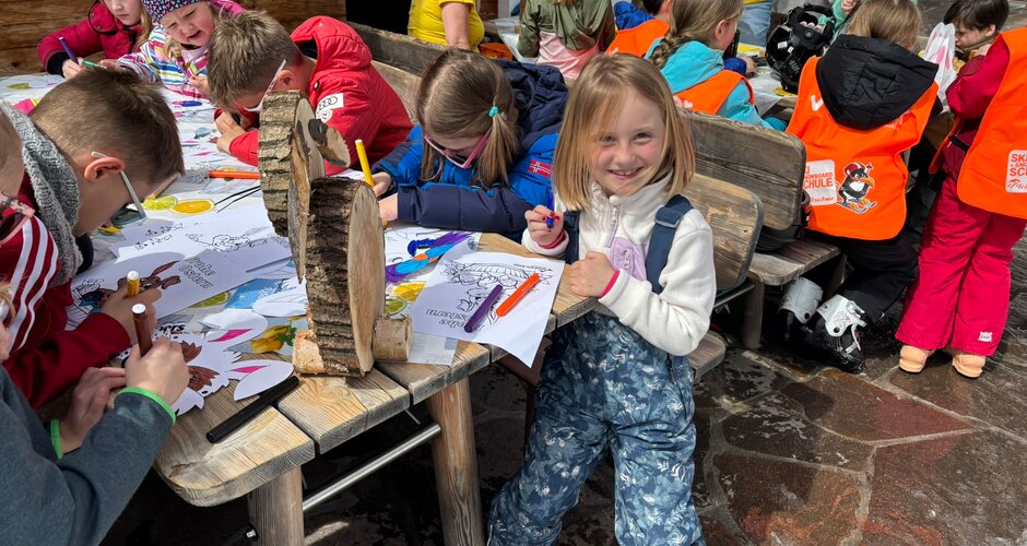 Mehrere Kinder sitzen an Holztischen und malen Ausmalbilder bei einem Kinderprogramm im Skigebiet | © Planai