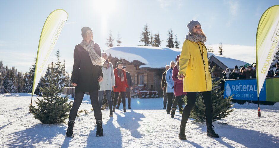 Modenschau im Schnee auf der Reiteralm bei strahlendem Sonnenschein | © Gerald Grünwald Mehrere Models präsentieren Wintermode im Schnee vor einer Hütte auf der sonnigen Reiteralm | © Gerald Grünwald