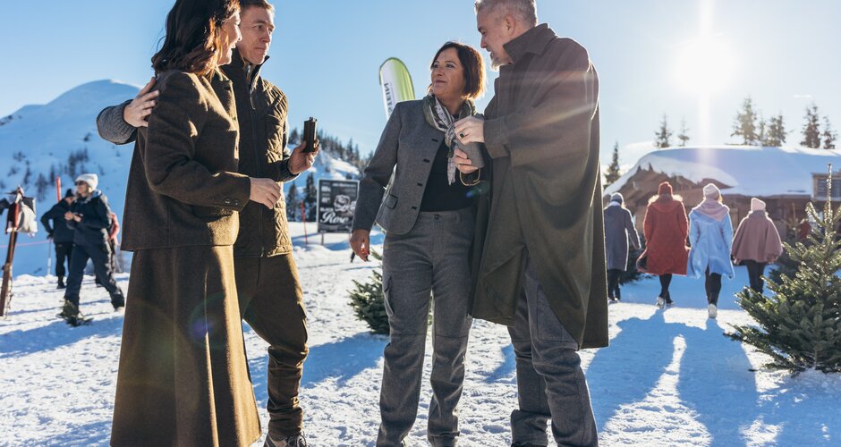 Gespräche und Wintermode auf der Reiteralm bei Sonnenschein | © Gerald Grünwald Vier Personen unterhalten sich in Wintermode im Schnee, weitere Models gehen im Hintergrund vorbei | © Gerald Grünwald