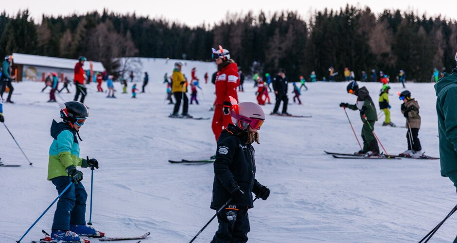 Viele Kinder fahren bei Dämmerung in Gruppen Ski auf der Reiteralm, begleitet von Skilehrern | © Gerald Grünwald