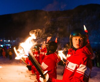 Junge Fackelträger in roter Skibekleidung stehen im Schnee bei nächtlicher Silvestershow bereit | © Gerald Grünwald