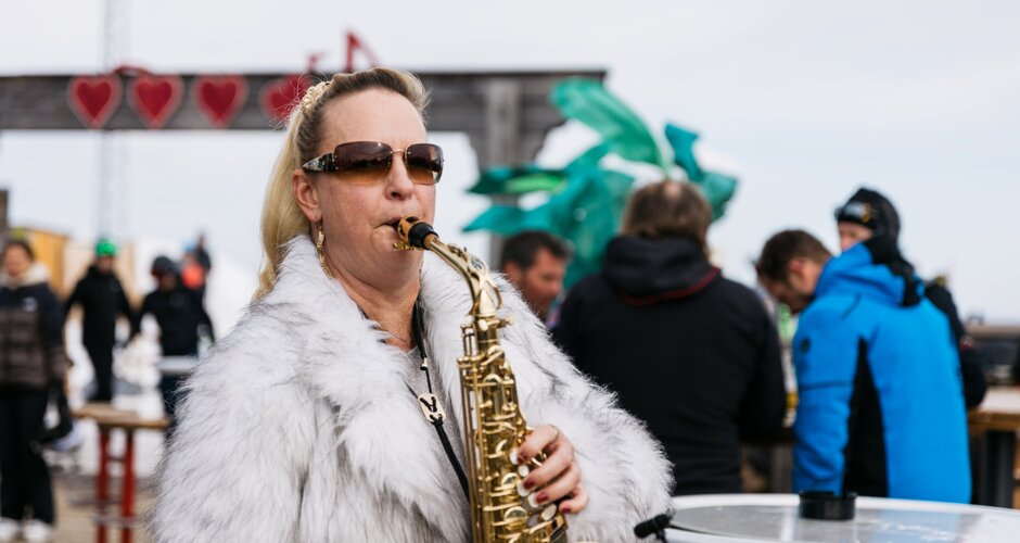 Frau mit Sonnenbrille und Felljacke spielt Saxofon bei Outdoor-Event auf der Reiteralm | © Gerald Grünwald