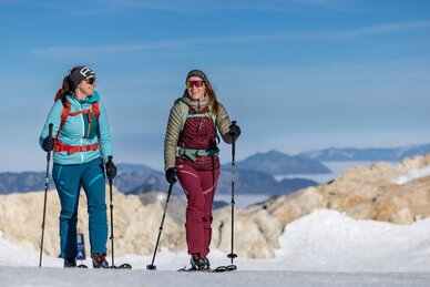 Zwei Frauen gehen mit Skitourenausrüstung und Stöcken durch sonnige Schneelandschaft | © Harald Steiner