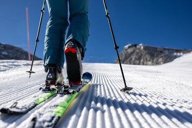 Nahaufnahme eines Tourenskischuhs auf gespurer Piste mit Stöcken und Sonne im Hintergrund | © Harald Steiner