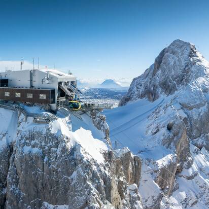Eine moderne Bergstation mit Seilbahn auf einem schneebedeckten Gipfel, umgeben von einer beeindruckenden Berglandschaft. | © Josh Absenger