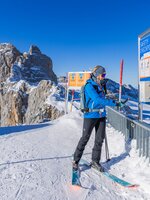 Skier checks avalanche transceiver at safety checkpoint with rocky mountain backdrop. | © René Eduard Perhab