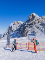 Two winter sports enthusiasts at a training area with flags, fence and mountain backdrop on Dachstein Glacier. | © René Eduard Perhab