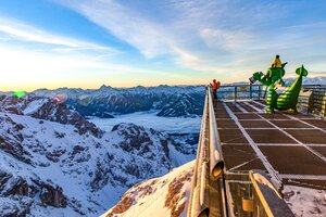 Schneebedeckte Berge, Mann auf Aussichtsplattform und grüne Drachenfigur am Dachstein. | © Renè Eduard Perhab