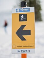 Gelbes Skitouren-Schild mit Pfeil zur Goliath-Schaukel auf der Fageralm im Schnee