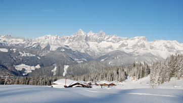 Verschneite Berghütten und Alpenpanorama mit tief verschneiten Bäumen auf der Fageralm.