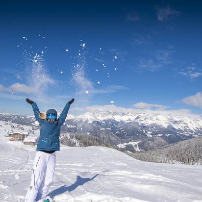 Frau wirft lachend Schnee in die Luft, mit Bergen und verschneitem Tal im Hintergrund. | © Lorenz Masser