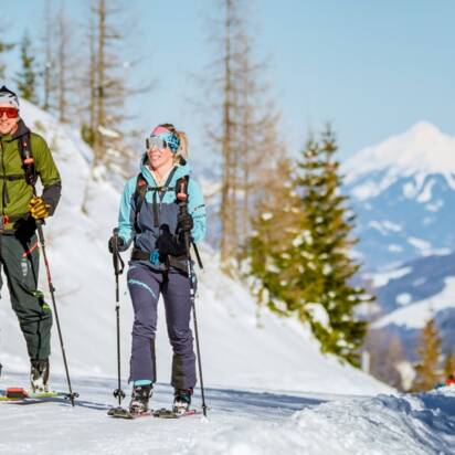 Zwei Skitourengeher steigen eine verschneite Piste am Galsterberg hinauf, während eine rote Gondel über ihnen schwebt. | © Christoph Huber