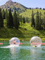 Zwei Kinder in transparenten Zorbing-Bällen auf einem See vor grüner Bergkulisse. | © Hauser Kaibling