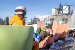 Zwei Skifahrer entspannen in orangefarbenen Liegen auf der Genussinsel im Schnee. | © Bernhard Moser