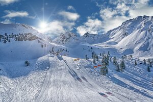 Skipiste mit orangefarbenen Sesselliften, Sonne und verschneiten Bergen am Hauser Kaibling.