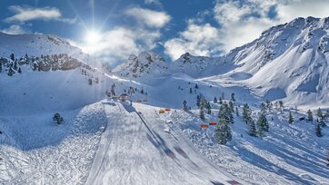 Skipiste mit orangefarbenen Sesselliften, Sonne und verschneiten Bergen am Hauser Kaibling.