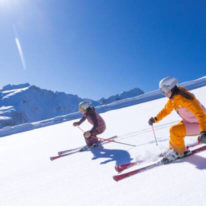 Zwei Skifahrer fahren bei Sonne auf präparierter Piste mit frischem Neuschnee. | © Hauser Kaibling